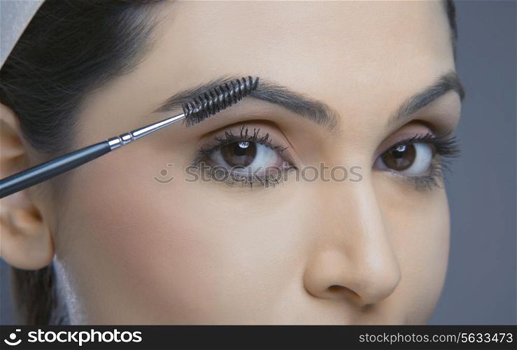 Close-up of young woman with eyebrow tinting applicator over colored background