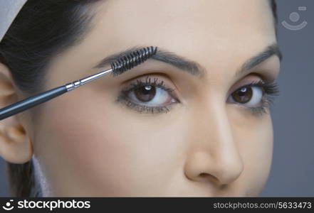 Close-up of young woman with eyebrow tinting applicator over colored background
