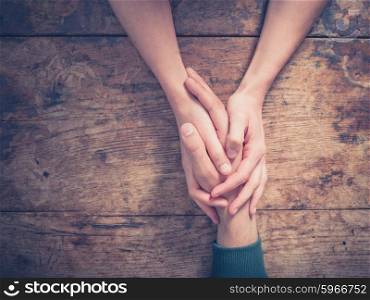 Close up on a man and a woman holding hands at a wooden table