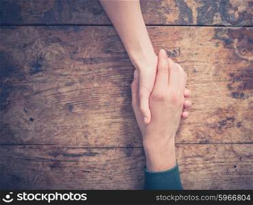 Close up on a man and a woman holding hands at a wooden table