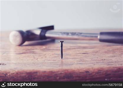 Close up on a nail in a table with hammer in background