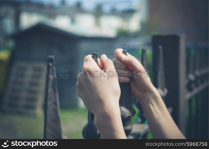 Close up on a woman&rsquo;s hands as she is holding onto a fence outside a yard with a shed