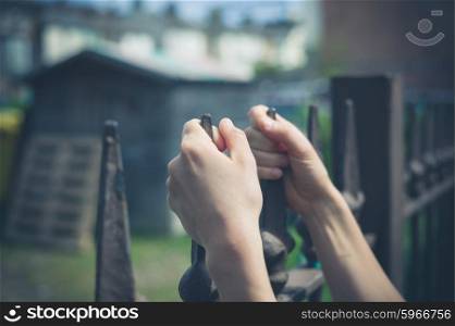 Close up on a woman&rsquo;s hands as she is holding onto a fence outside a yard with a shed