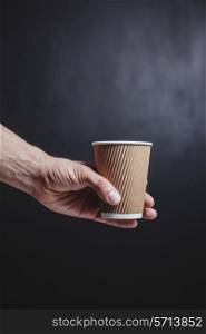 Close up on a young man&rsquo;s hand holding a brown paper cup