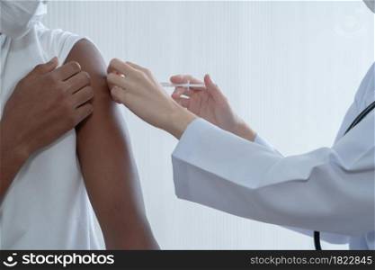 Close up on Asian woman doctor hand holding syringe to injections or vaccines to upper arm of African dark skinned man. White background. Preventing spread of COVID-19 by vaccinating people concept
