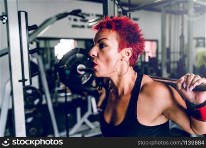 Close up on caucasian woman red short hair training at the gym lifting weight leg workout squats holding barbell powerlifting fitness