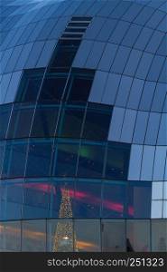 Close-up on exterior glass of Sage Gateshead concert hall on Newcastle Gateshead Quayside with visible illuminated Christmas tree