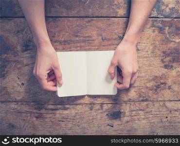 Close up on female hands opening a small notepad at a wooden table