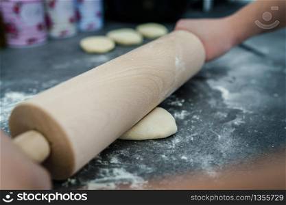 Close up on hand of unknown caucasian woman female girl making bread knead the dough kneading on the kitchen table at home top view using rolling pin