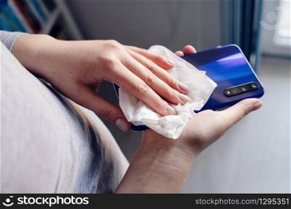Close up on hands of caucasian young woman female holding mobile smart phone in hand wiping cleaning screen disinfection with white wet wipe towel napkin alcohol anti virus and bacteria prevention