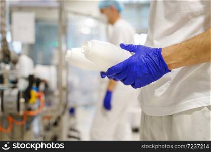 Close up on hands of unknown caucasian man holding bottle container while working at factory - Food production blue rubber protective gloves on hands as hygiene procedure at work - safety concept