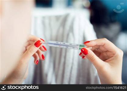 Close up on hands of unknown caucasian woman holding thermometer while lying in bed - Adult female checking and measuring body temperature having fever at home - Covid-19 pandemic concept healthcare