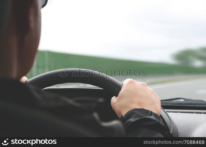 Close-up on male hands on the steering wheel of a car on a blurred background of the highway (reduced tone effect)