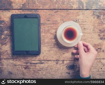 Close up on male hands with a cup of coffee and a tablet computer on a wooden table