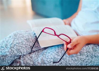 Close up on midsection of girl or woman holding a book and glasses while reading sitting on the floor at home