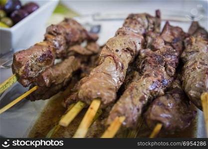 Close up on shashlik (lamb) meat with wooden skewer that is on white plate.