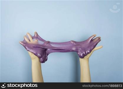 Close up on shiny purple or violet slime in the hand isolated on blue background. Fun and stress relief concept.. Close up on shiny purple or violet slime in the hand isolated on blue background. Fun and stress relief concept
