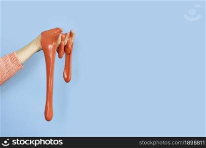 Close up on shiny Red or coral slime in the hand isolated on blue background. Fun and stress relief concept. Banner with copy space.. Close up on shiny Red or coral slime in the hand isolated on blue background. Fun and stress relief concept. Banner with copy space