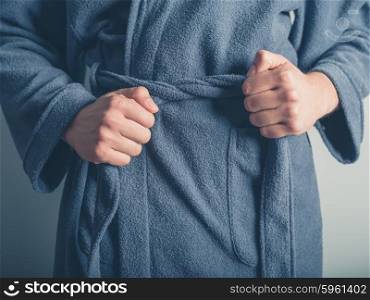 Close up on the hands of a man as he is tying the belt of his bathrobe