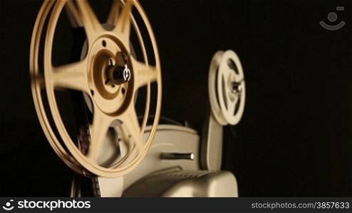 Close-up on the spinning film reels of an antique 8mm film projector in a dark room. Includes projector audio