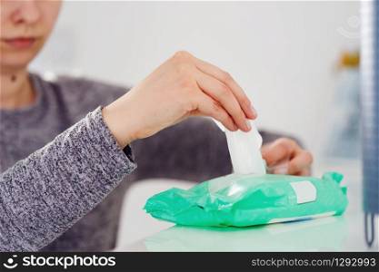 Close up on woman&rsquo;s hands unknown female hand taking wet napkin towel tissue from the box container package on the white shelf at home or office antibacterial disinfection alcohol hygiene product