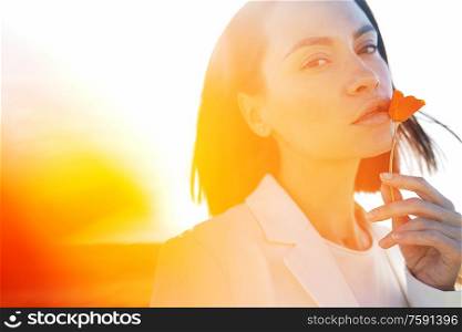 Close up outdoor lifestyle portrait of beautiful young woman with poppy flower in hand. Freedom and independence.Soft colors.