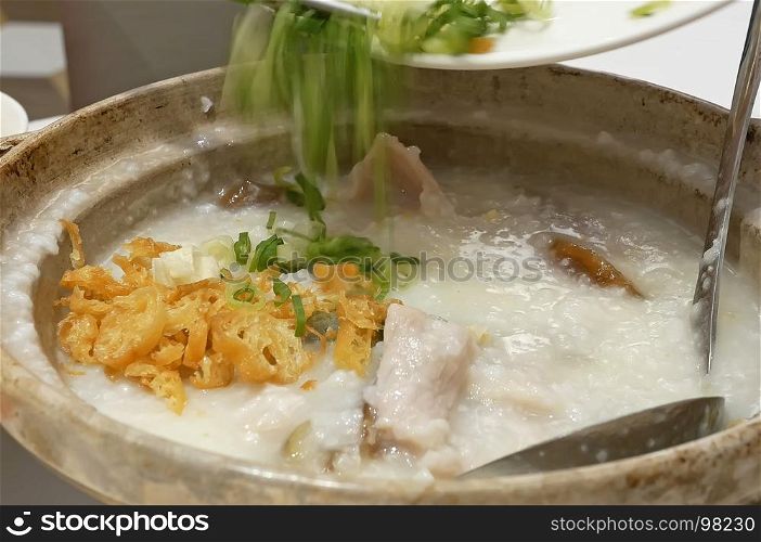 Close up people pouring green onion inside minced pork congee with preserved egg on table