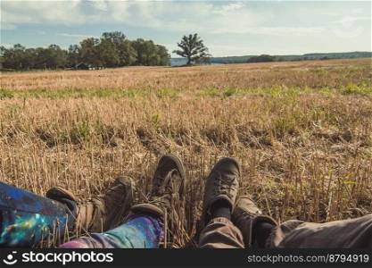Close up people sitting on dry grass in field concept photo. First view person photography with cloudy sky on background. High quality picture for wallpaper, travel blog, magazine, article. Close up people sitting on dry grass in field concept photo