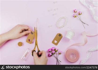 close up person cutting tag with bracelet artificial roses ribbon pink background