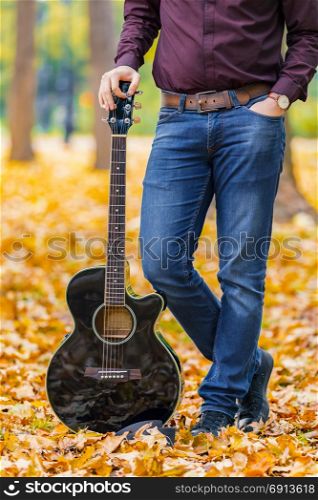 Close up person man?s hands on acoustic guitar in autumn park. Focus on guitar.
