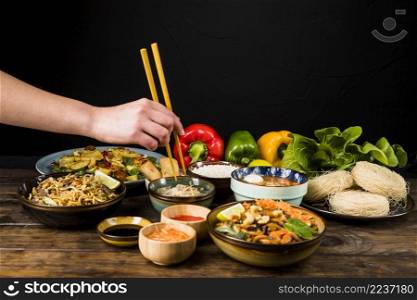 close up person s hand eating thai food with chopsticks table against black backdrop