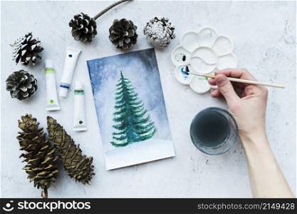 close up person s hand painting christmas tree with acrylic paint tubes