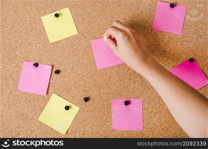 close up person s hand putting blank notepad cork board with push pin