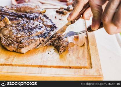 close up person s hand slicing meat with fork knife