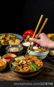 close up person s hand taking thai food with chopsticks against black background