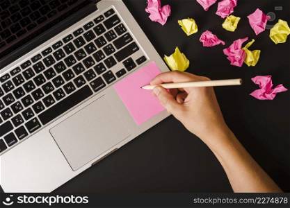 close up person s hand writing pink adhesive note laptop against black background