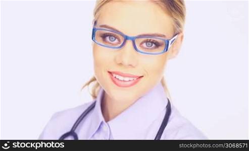 Close up pf the face of a beautiful young female doctor in trendy glasses and a stethoscope smiling at the camera