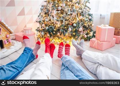 Close up photo of family feet in woolen socks by the christmas tree. Family of four on Christmas Holiday. Close up photo of family feet in woolen socks by the christmas tree