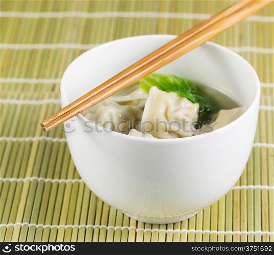 Close up photo of freshly made wonton with chopsticks on top of white bowl