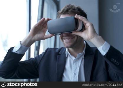 Close up photo of happy excited business person in suit wearing VR headset on head taking part in meeting in virtual reality, smiling young businessman using innovative technology 3d glasses in office. Excited business person in suit wearing VR headset on head taking part in meeting in virtual reality