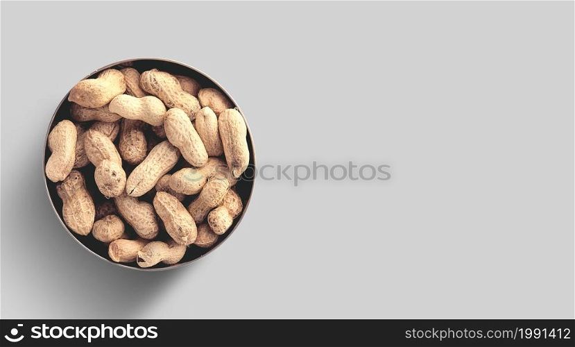 Close up photo of top view peanuts added on ceramic bowl, raw peanuts in the nutshells isolated on grey background.