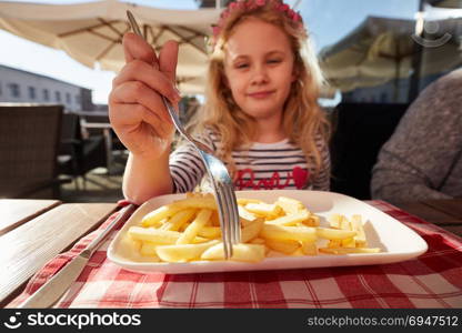Close up photo preschool girl eats french fries potatoes sitting in cafe outdoors.. Close up photo preschool girl eats french fries potatoes sitting in cafe outdoors