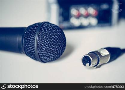 Close up picture of a black microphone and audio cable, mixer in the blurry background
