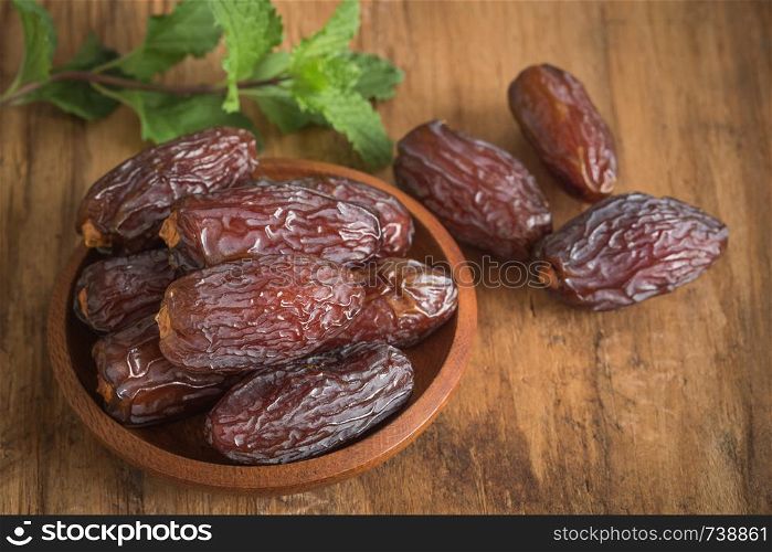 close up picture of dates palm fruit in cup and mint on wooden table background. Dates palm fruit dry is snack healthy.