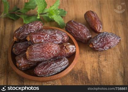 close up picture of dates palm fruit in cup and mint on wooden table background. Dates palm fruit dry is snack healthy.
