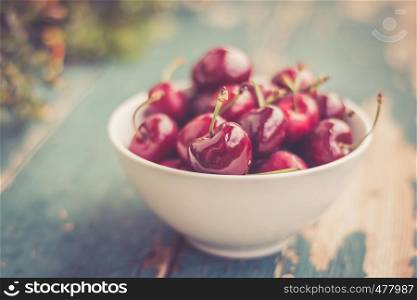 Close up picture of fresh red strawberries lying in a white bowl on a rustic table, outdoors