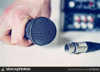 Close up picture of holding in hand microphone and audio cable, mixer in the blurry background