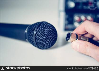 Close up picture of holding in hand microphone and audio cable, mixer in the blurry background