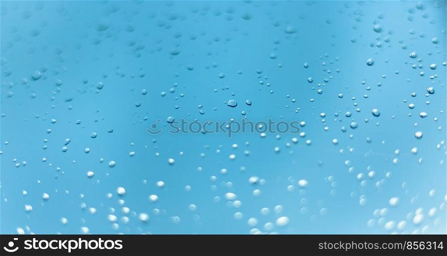 Close up picture of water drops on the window. Blue sky and clouds in the background.