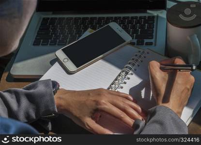 Close-up pictures of young women who are taking notes of work On a table made with a laptop, a mobile phone and a cup of coffee placed next to